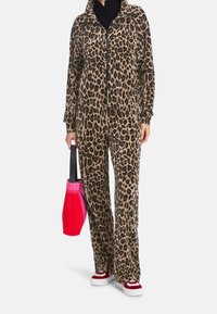 Dres w panterkę w odcieniach brązu, składający się z rozpinanej kurtki i luźnych spodni, połączony z różową i czerwoną torebką oraz casualowymi butami.