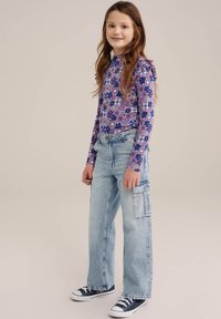 Cămașă mov cu mânecă lungă și model floral, combinată cu blugi cargo de un albastru deschis, având buzunare mari și o textură decolorată, purtată cu teniși navy.