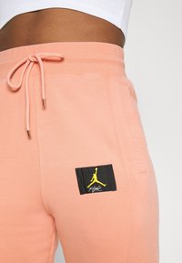 Peach-colored sweatpants made of soft fabric, featuring a black patch with a yellow Air Jordan logo and text "Flight" on the side.