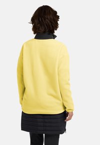 Pullover in fleece giallo con colletto nero, caratterizzato da una vestibilità rilassata e una texture liscia, abbinato a una gonna imbottita nera.