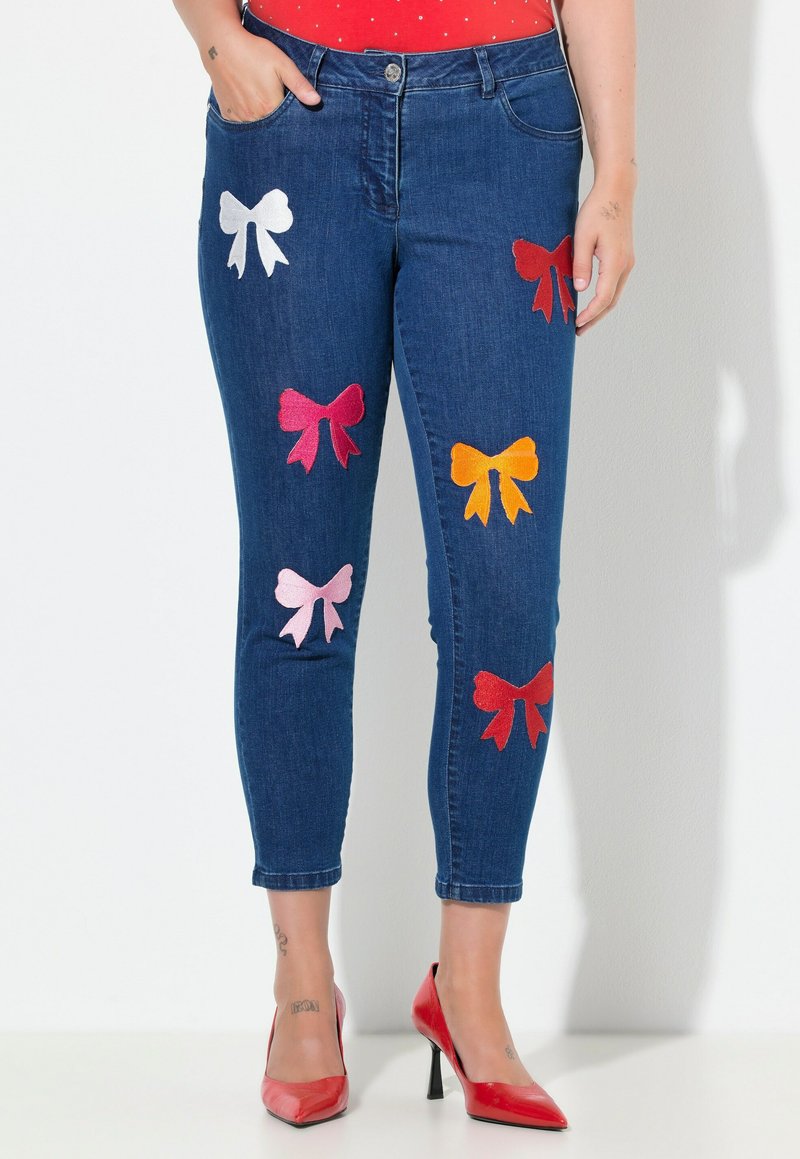 Džínové kalhoty s přiléhavým střihem, zdobené barevnými vyšívanými mašličkami v růžové, červené, bílé a oranžové barvě. Klasický design s pěti kapsami, ohrnutý lem.