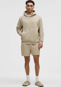 Beige huppari, jossa on kengurun tasku, yhdistettynä matching-shorteihin. Pehmeä kangas, rento malli ja minimalistinen muotoilu.