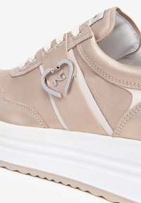 Baskets en rose doré métallisé avec des accents blancs, cuir texturé, bout rond, détail d'un logo en forme de cœur argenté et une semelle blanche épaisse.