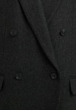 Blazer en laine noir à chevrons, doté d'une fermeture double boutonnage avec quatre boutons noirs et de revers crantés. Tissu texturé.