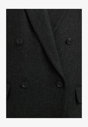 Blazer de lana negro en patrón espiga, con cierre de doble botonadura y cuatro botones negros, además de solapas con muesca. Tejido texturizado.