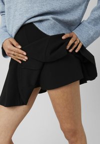 Shorts noirs avec un design en volants superposés, fabriqués dans un tissu lisse. La ceinture est structurée, avec des détails de couture subtils.