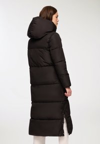Długi czarny puchowy płaszcz z kapturem, charakteryzujący się pikowanym wzorem. Płaszcz ma prosty krój oraz boczne zamki na dole, co zapewnia możliwość regulacji.
