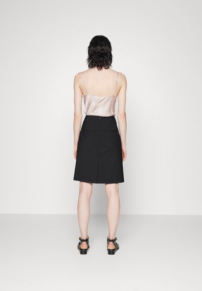 Jupe noire à coupe droite, avec poches arrière et couture centrale ; associée à un débardeur en satin pâle avec des bretelles fines.