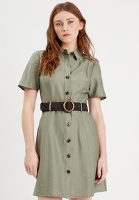 Olivgrünes Hemdkleid mit kurzen Ärmeln, Knopfleiste, einem schwarzen Gürtel mit einer hölzernen Schnalle und einer strukturierten Stoffoberfläche.