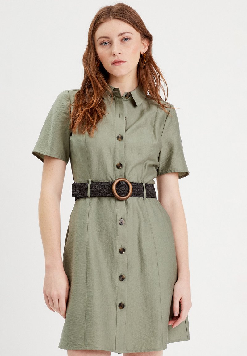 Olivgrünes Hemdkleid mit kurzen Ärmeln, Knopfleiste, einem schwarzen Gürtel mit einer hölzernen Schnalle und einer strukturierten Stoffoberfläche.