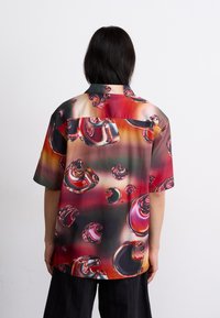 Chemise à manches courtes ornée d'un motif abstrait de bulles colorées sur un tissu satiné, dégradé de rouge à vert.