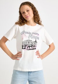 Hvid bomulds-T-shirt med et grafisk design af en pariser café, med pink blomsteraccenter og stiliseret tekst "Paris mon Amour."
