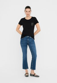 Sort kortærmet T-shirt med en lomme, der har et tekstureret design, parret med blå lige ben jeans og mønstrede sorte flade sko.