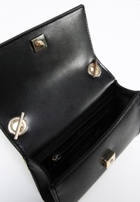 Invändig del av en svart läderhandväska som har en slät textur, guldhandtag och ett blixtlåsfack med kortfack.