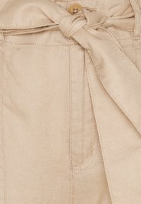 Beige linne tyg med en strukturerad yta, med en knuten bältesdetalj, en knappstängning och sydda fickor.