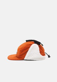 Orange corduroy cap with a white fluffy fabric accent. Features a flexible brim and a black adjustable strap at the back.
