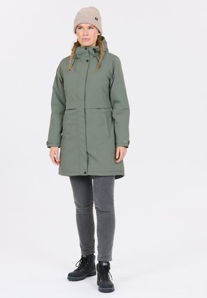 Olivgrön vattentät parka med dragsko i huvan, framfickor och rak passform; kombinerad med grå jeans och svarta snörstövlar.