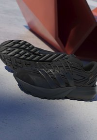 Čierne športové topánky majú štruktúrovaný zvršok, viacpanelový dizajn, hrubú gumovú podrážku s hlbokým dezénom a šnúrky pre bezpečné uchytenie.