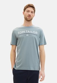 Světle modré bavlněné tričko s krátkými rukávy, se značkovým logem "TOM TAILOR" a designem "1962" v kontrastních bílých a tmavě modrých barvách.