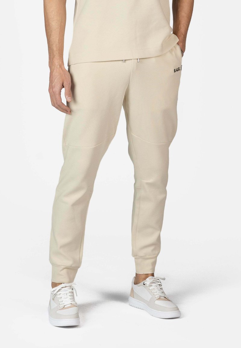 Pantaloni de trening bej cu croială conică, manșete elastice, buzunare laterale și un logo subtil. Asociați cu adidași albi cu accente bej deschis.