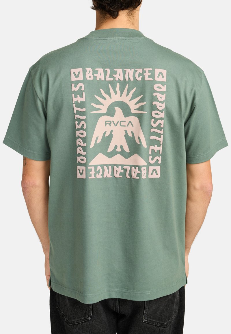 Green cotton t-shirt featuring a pink graphic design on the back, with the text "BALANCE OPPOSITES" and an eagle graphic above mountains.