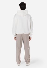 Sweatshirt branco com capuz e corte relaxado. Tecido suave, punhos canelados e bolso tipo canguru. Combinado com calças bege e sapatilhas brancas.