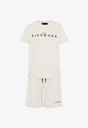 Ensemble t-shirt blanc et short avec le texte "John Richmond" imprimé sur la poitrine et sur la jambe gauche du short.
