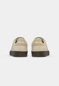 Sneaker in suede beige con suola in gomma marrone, caratterizzate da un tassello sul tallone color corda e logo "VEJA" bianco sul retro. Design minimalista, forma a profilo basso.