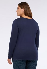Langärmliges, navyblaues Oberteil aus weichem Stoff mit Rundhalsausschnitt und lockerer Passform, das seitliche Schlitze am Saum für zusätzliche Details aufweist.