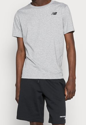 Szara bawełniana koszulka z okrągłym dekoltem i krótkimi rękawami, z czarnym logo na piersi, zestawiona z ciemnymi szortami.