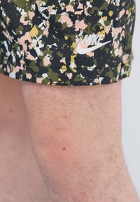 Nike shorts with a black, green, pink, and white abstract pattern; includes a white embroidered logo. Made from smooth fabric.