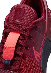 Chaussure de sport rouge avec tige en maille texturée, lacets épais, grand onglet de tirage sur la languette et semelle noire à motif.