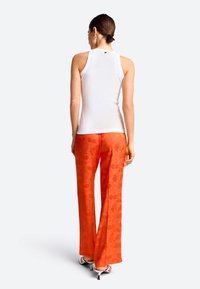 Weißes rippenförmiges Tanktop kombiniert mit orangefarbenen, blumenmusternden Hosen. Das Outfit zeichnet sich durch ein eng anliegendes Design und eine glatte Stoffstruktur aus.