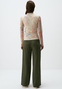 Top floreale a maniche lunghe in crema con fiori rosa e blu, abbinato a pantaloni larghi verde oliva, dotati di design con tasca sul retro.