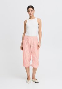 Pantalons cropped légers en rose pâle, amples, avec une taille élastique et un détail de cheville froncé, associés à un haut sans manches blanc.