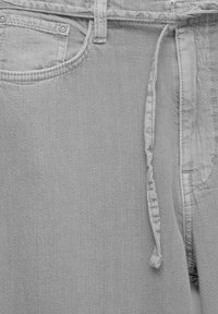 Helle graue Denim-Hosen mit verstellbarem Kordelzug in der Taille, Fronttasche und gestickten Details. Weiche Textur, lässiges Design.