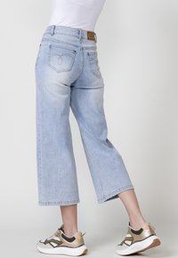 Jeans de pierna ancha azul claro con una cintura de talle medio y bolsillos traseros bordados, combinados con zapatillas deportivas blancas y doradas.