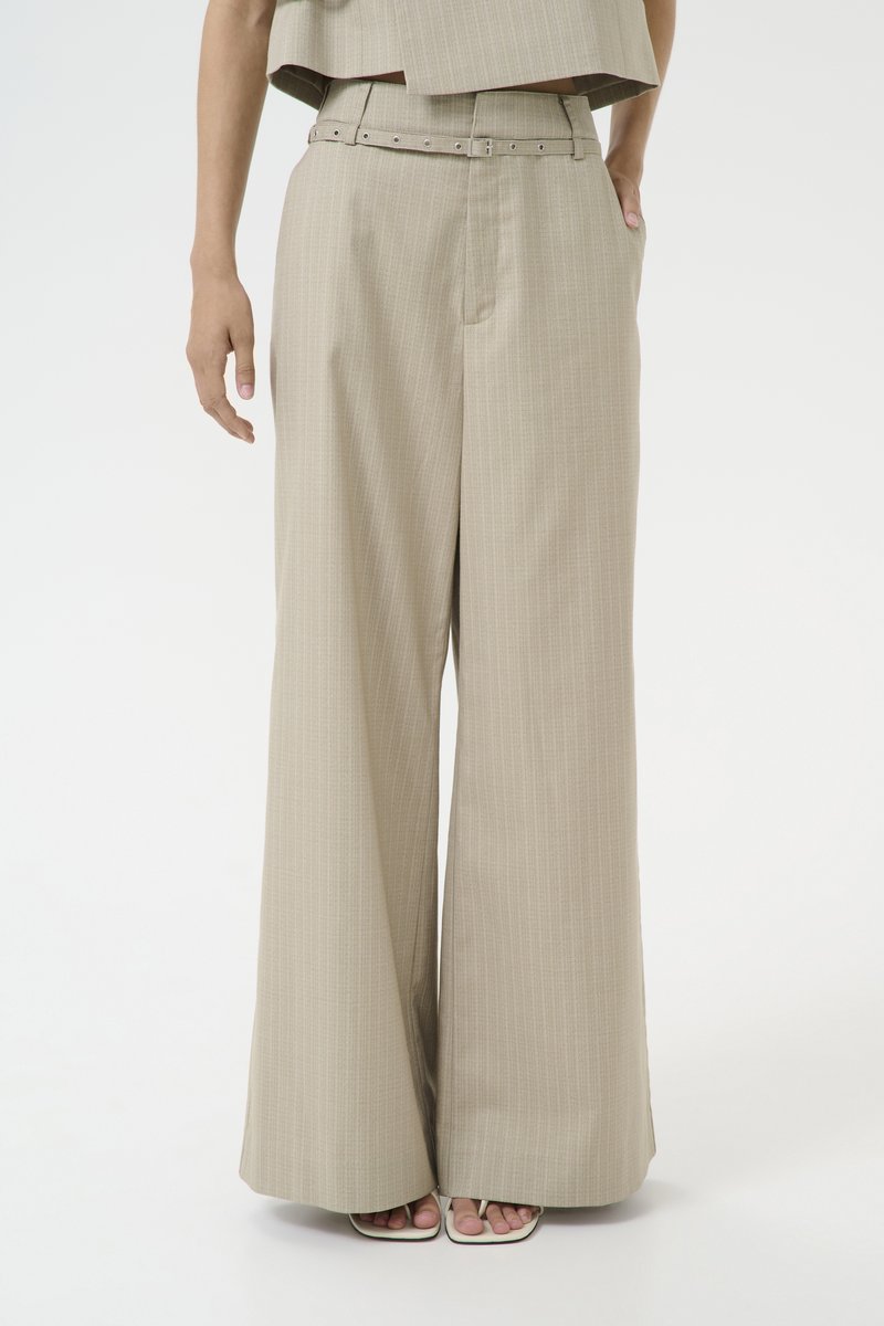 Lys beige vide benbukser med et pinstripe-mønster, belted midje og sidelommer; parret med hvite stroppesandaler.