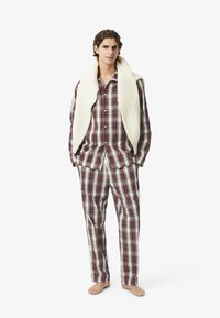 Piros és fehér kockás flanel pizsama gombos inggel és egyeztetett nadrággal. Egy textúrált krém színű pulóvert adtak a vállakra.