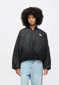 Czarna kurtka bomberka z przednim zamkiem błyskawicznym, prążkowanym kołnierzem i kieszeniami po bokach. Posiada logo na piersi oraz gładki, lekki materiał.