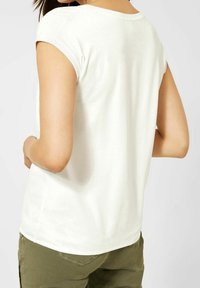 Vit kortärmad topp med mjuk textur, rundad halsringning och en något avslappnad passform, tillsammans med olivgröna byxor.