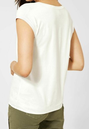 Top blanco de manga corta con una textura suave, cuello redondeado y un ajuste ligeramente relajado, combinado con pantalones verdes oliva.
