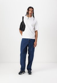 Hvit bomulls T-skjorte, løstsittende blå denimjeans, svart crossover-veske, svarte joggesko, rett snitt-design, minimale detaljer.