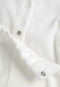 Garbamento bianco con una texture di tessuto morbido, bottoni a scatto e dettagli con bottoni arrotondati lungo la parte anteriore e i polsini.