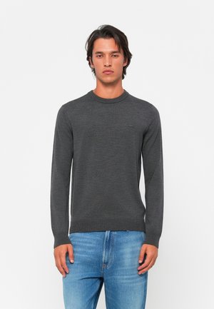 Dark grey, long-sleeve sweater with a round neckline, made of knitted fabric. Subtle logo on the chest, paired with light blue jeans.