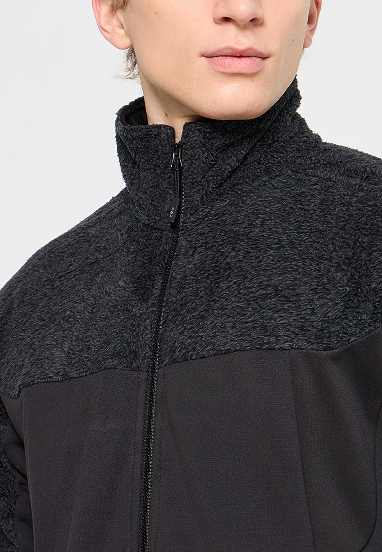 Giacca nera con zip, caratterizzata da una sezione superiore in pile texturizzato e una sezione inferiore liscia, con colletto alto e dettagli hardware minimi.