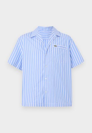 Gaiši zils īsām piedurknēm krekls ar pogām, baltām vertikālām svītrām un priekšējo kabatu, kurā ir mazs izšūts krokodila logo.