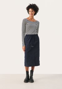 Gestreepte lange mouwen top in marineblauw en wit, gecombineerd met een marineblauwe geweven midi rok met een elastische tailleband en een trekkoord. Zwarte enkellaarsjes.