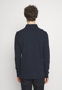 Granatowa koszulka polo z długim rękawem i kołnierzykiem. Miękka bawełniana tkanina, luźny krój oraz ściągacze przy mankietach. Prosty design, bez widocznych wzorów ani logo.