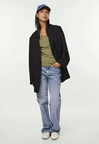 Μαύρη oversized σαλοπέτα, ελαιόχρωμο αμάνικο μπλουζάκι, ανοιχτό μπλε φαρδύ παντελόνι και λευκά αθλητικά παπούτσια. Το μπλε καπέλο συμπληρώνει την εμφάνιση.